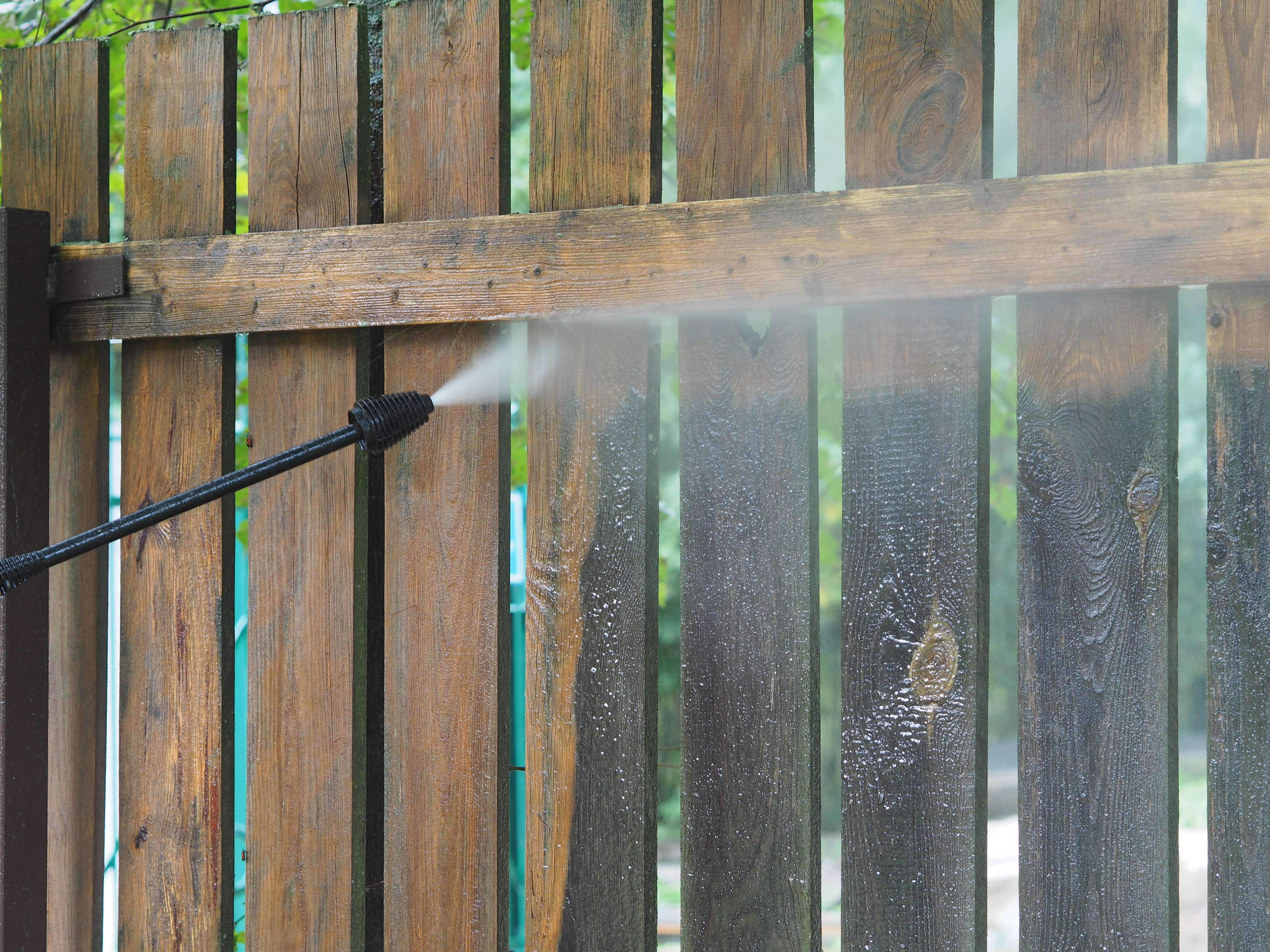 A close up of a 76 FENCE North Charlotte technician power washing a dirty fence.