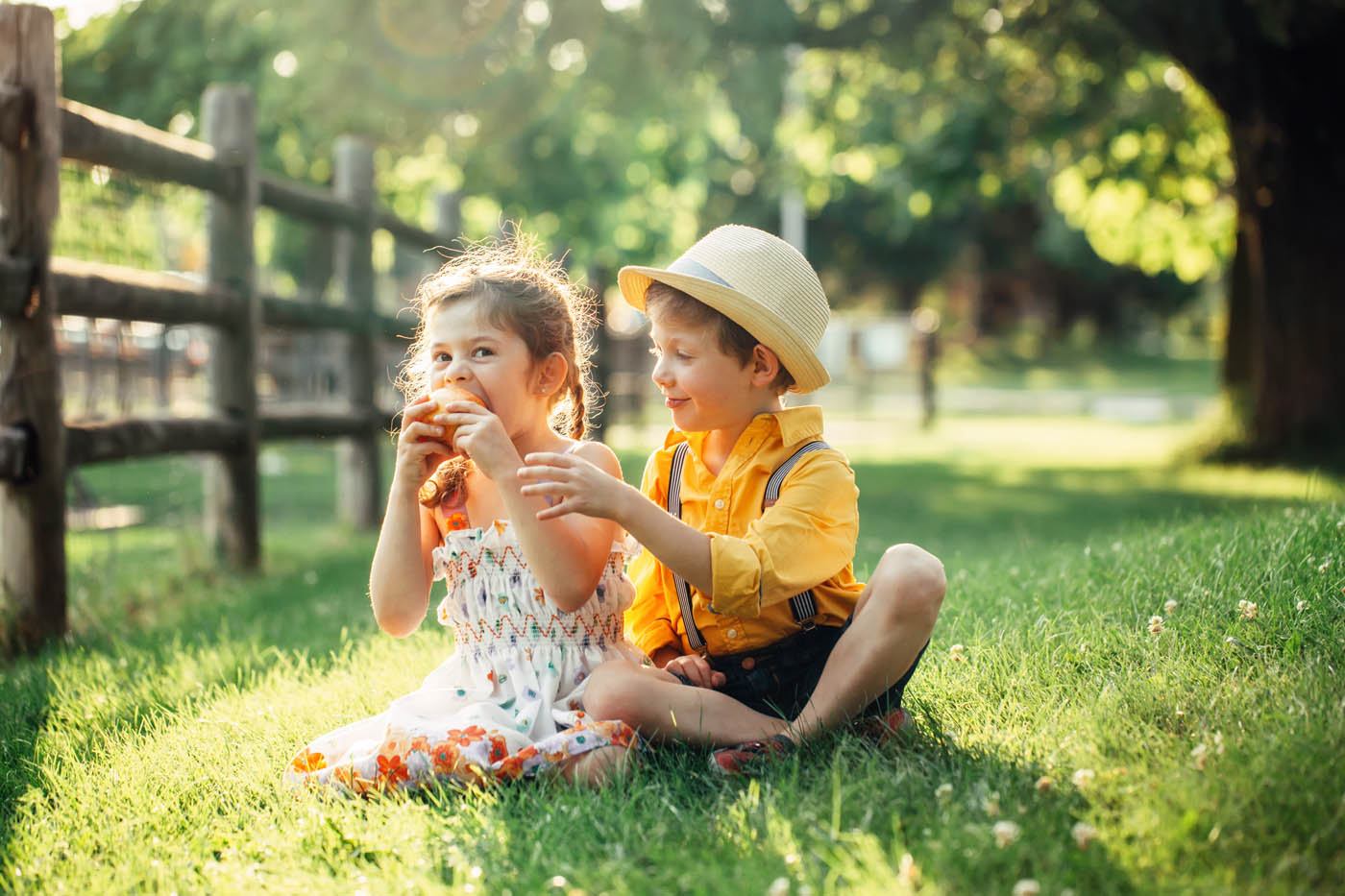 Kids sitting on the grass with a farm fencing.