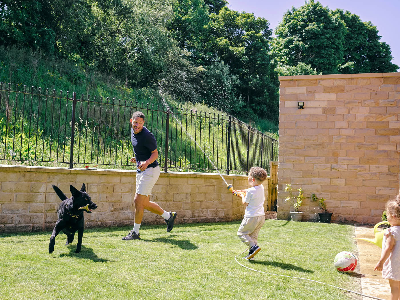 A father and young son running around their backyard with sprinklers, enjoying their refreshed backyard with 76 FENCE fence installation services in Schaumburg, IL.